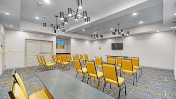 Sala de conferências com uma mesa comprida e várias cadeiras, luminárias no teto e sinal de saída.
