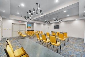 A conference room with a long table and multiple chairs, ceiling lights, and an exit sign.