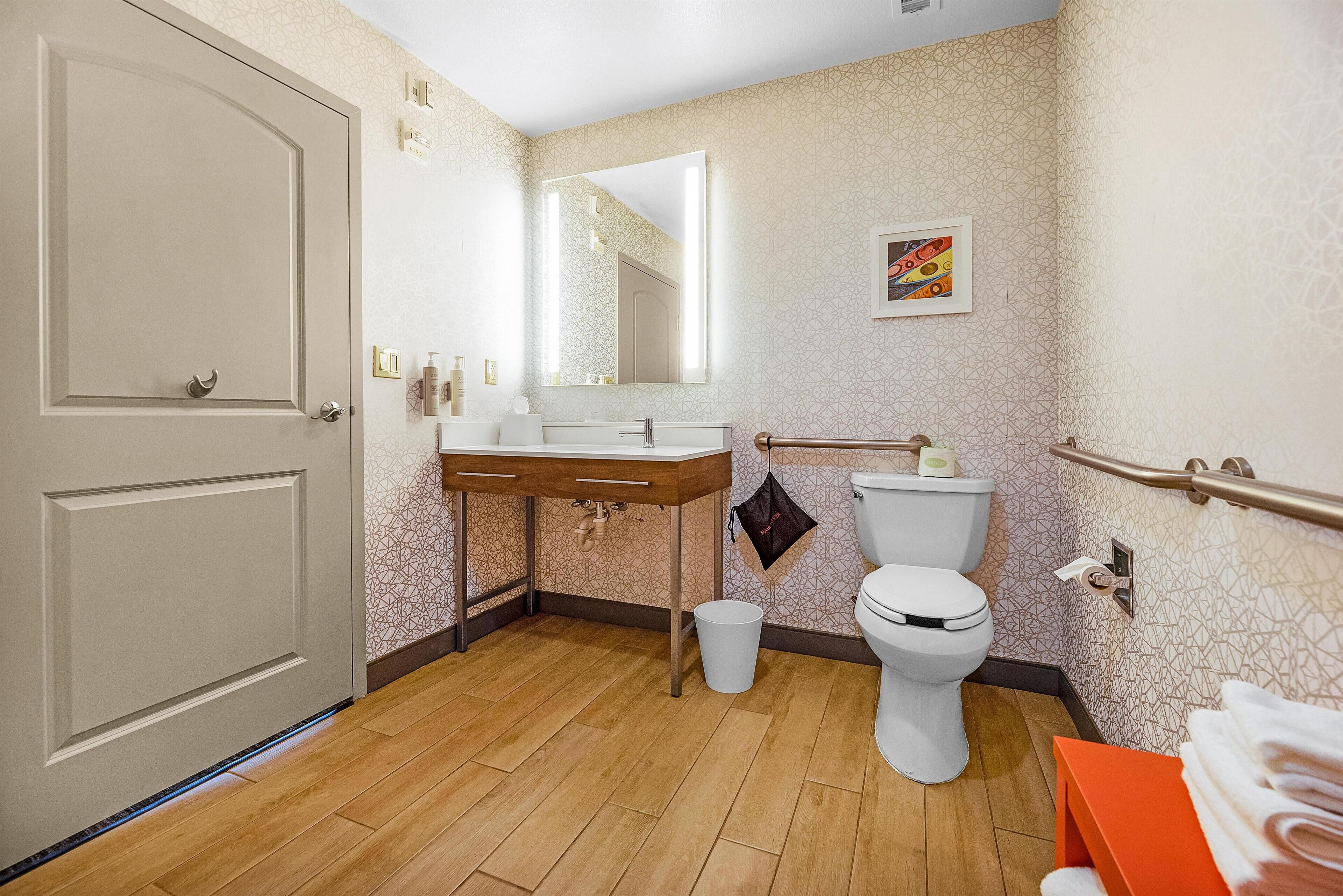 A bathroom with a wooden floor, a white toilet, a sink with a mirror, and a towel rack.
