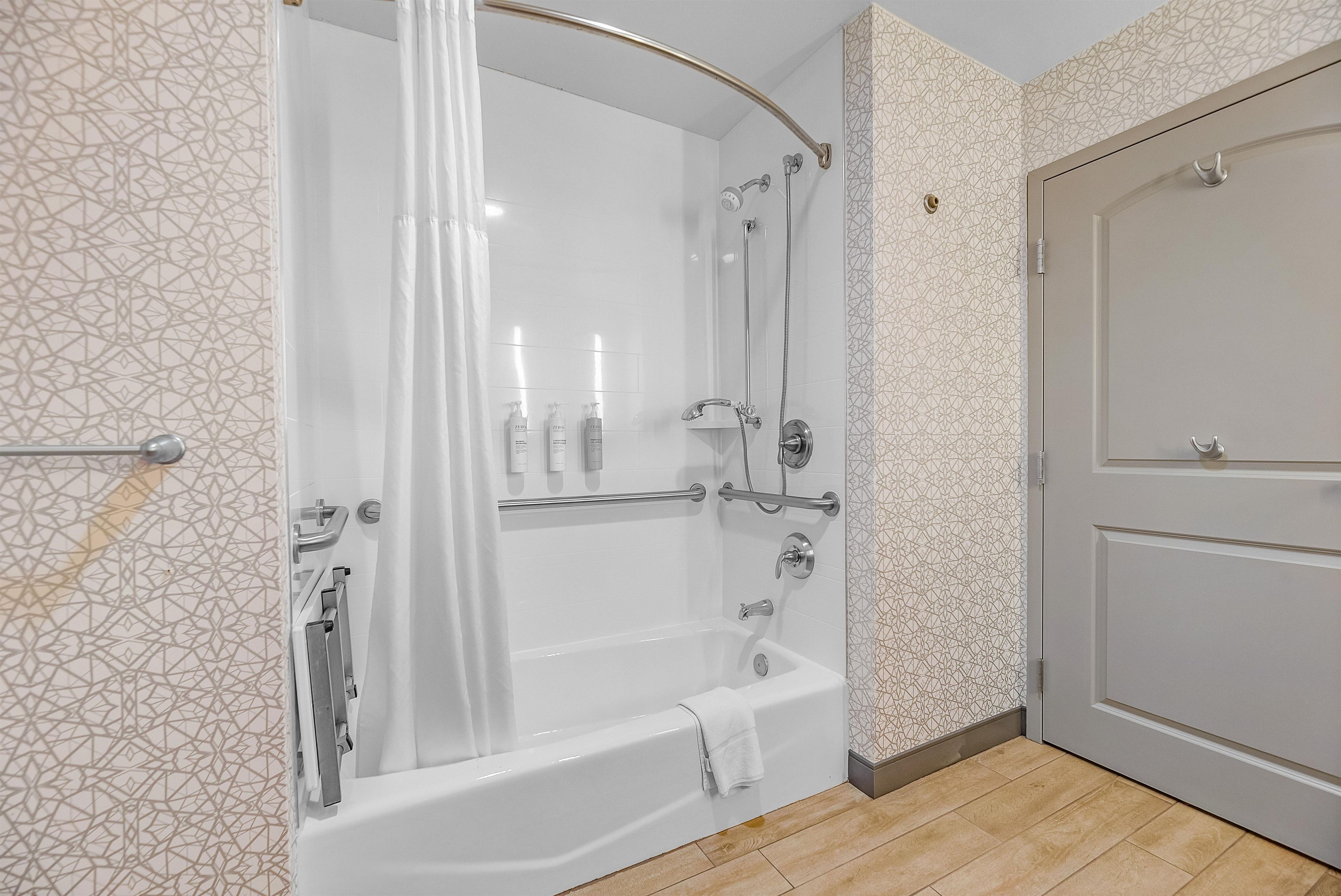 Ein modernes Badezimmer mit barrierefreier Dusche, einer Badewanne und einer Tür.