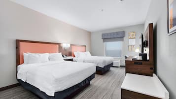A hotel room with two beds, a desk, a chair, a window, and a wall-mounted artwork.
