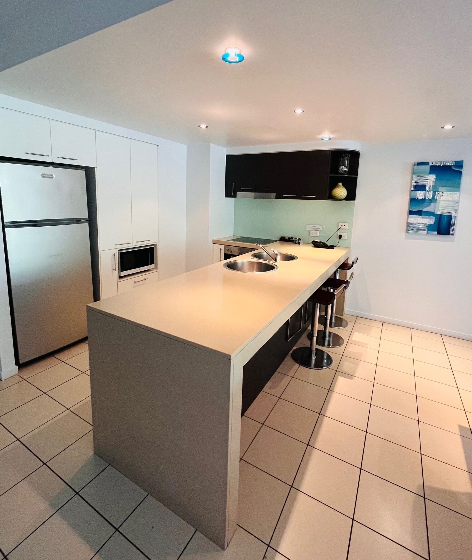 A modern kitchen with a large island, white cabinets, stainless steel appliances, and a tiled floor.