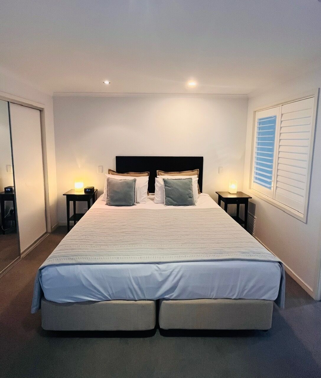 Ein Hotelzimmer mit einem großen Bett, zwei Nachttischen, einer Kopfteil und einem Fenster mit Jalousien.