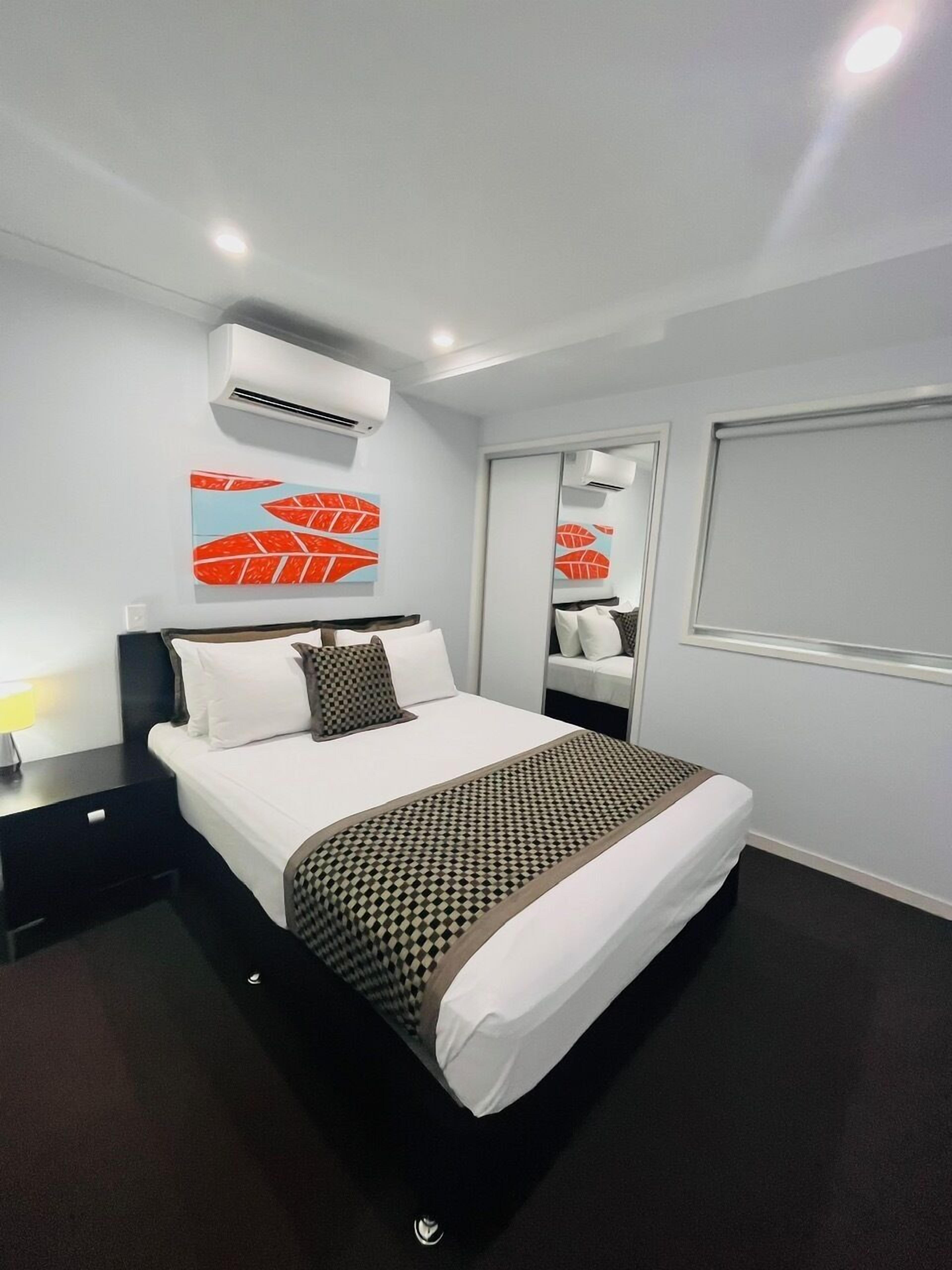 A modern hotel room with a large bed, a bedside table, an air conditioning unit, and a window with a view.
