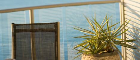 A balcony with a view of the sea, a wicker chair, a round table, and a potted plant.