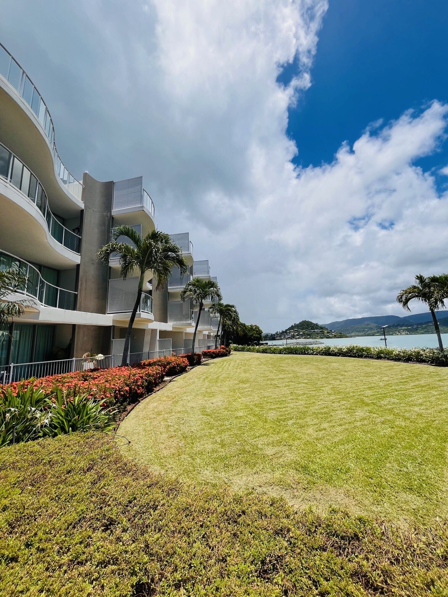 Un hotel moderno con un jardín curvo, palmeras y vista al mar.