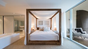 Un dormitorio moderno con una cama grande, cabecera de madera, lámparas de noche y vistas a un balcón con una silla.