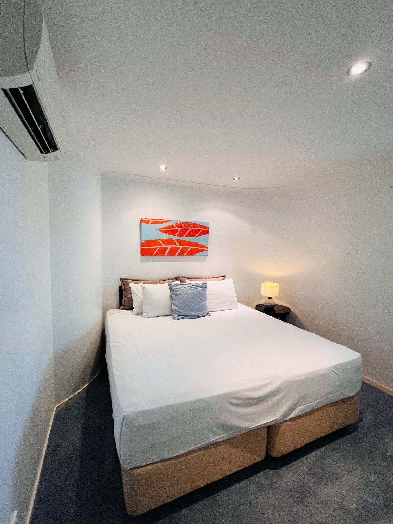 A hotel room with a single bed, a nightstand with a lamp, and a wall-mounted artwork.