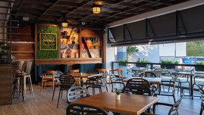 Interno di un ristorante con tavoli e sedie in legno, una parete verde decorata con opere d'arte e vista sulla strada.
