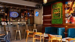 Un'area bar con sgabelli e un bancone, un divano blu e una parete con una pianta verde e un cartello.