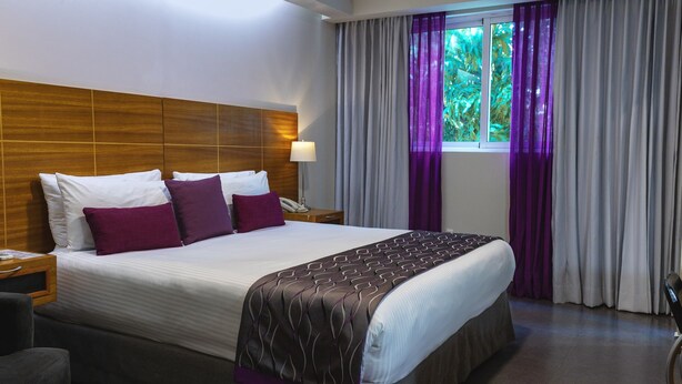 Camera d'albergo con un letto grande, una testiera in legno e una finestra con tende viola.