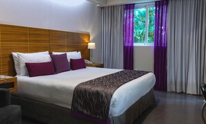 A hotel room with a large bed, wooden headboard, and a window with purple curtains. - Hotel Aladino (Santo Domingo)