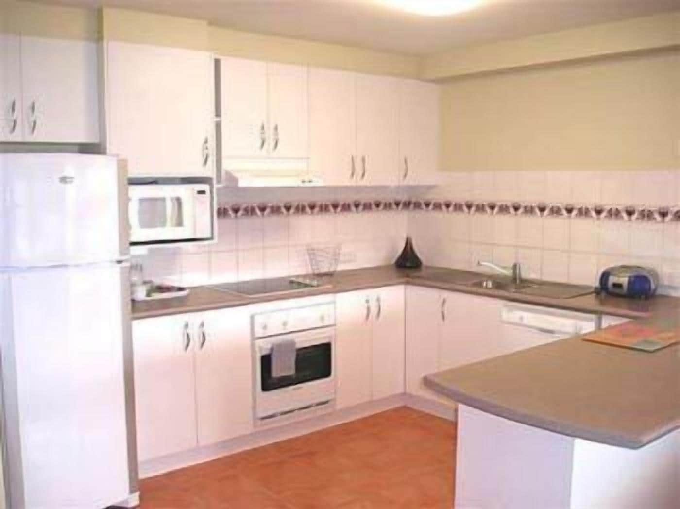 A compact kitchen with white cabinets, a microwave, an oven, and a sink.