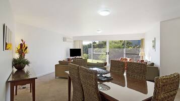 A modern living room with a dining table, wicker chairs, a sofa, and a television.