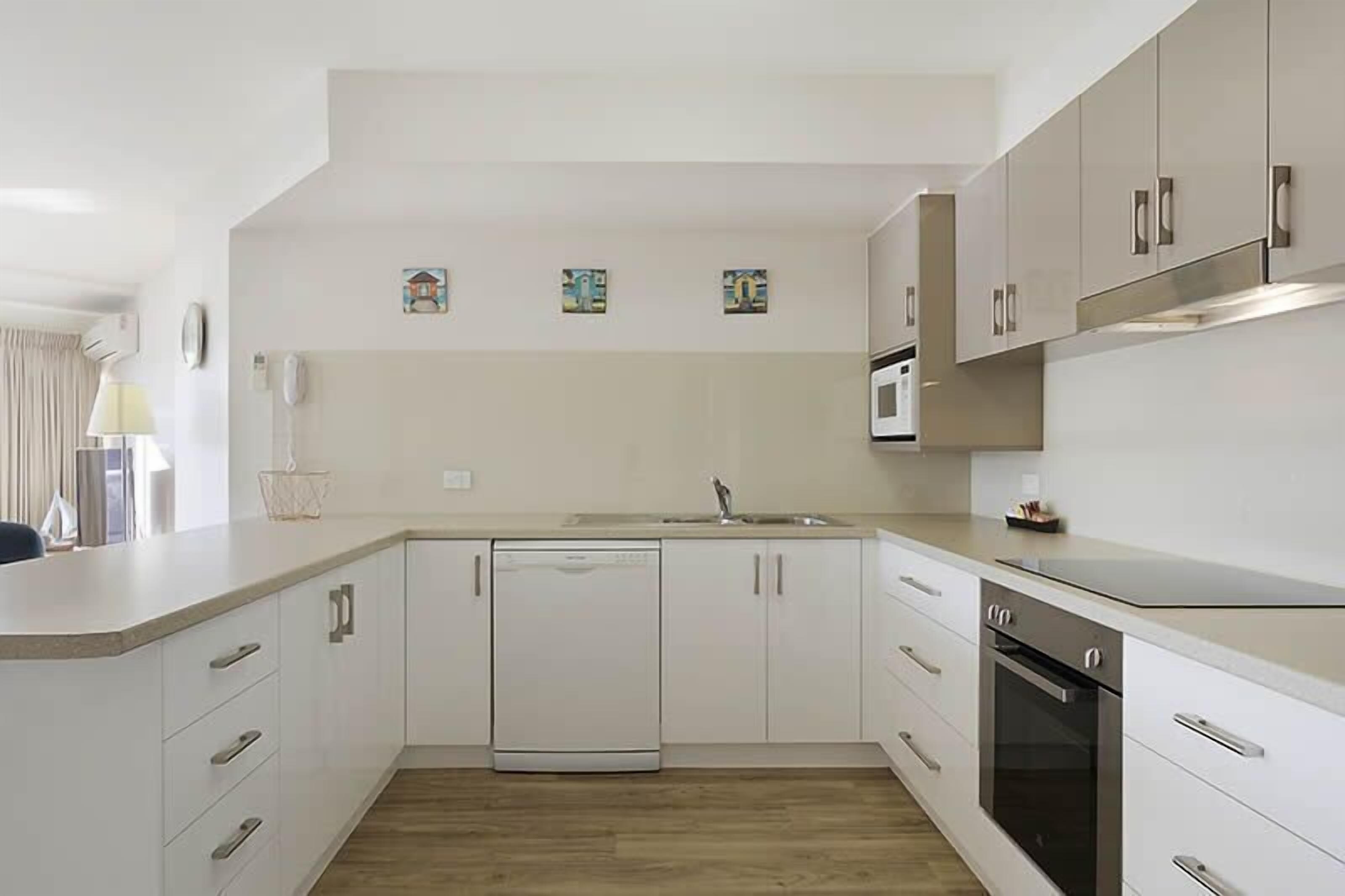 Una cocina moderna con armarios blancos, lavavajillas, horno y microondas.