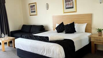 A hotel room with a bed, a sofa, a small table with glasses, and a potted plant.