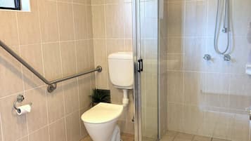 Un baño moderno con inodoro, cabina de ducha de vidrio y barra de apoyo.