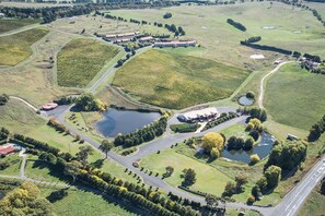 An aerial view of a vineyard with multiple rows of grapevines, several buildings, and a large body of water. - Turners Vineyard  (Orange)