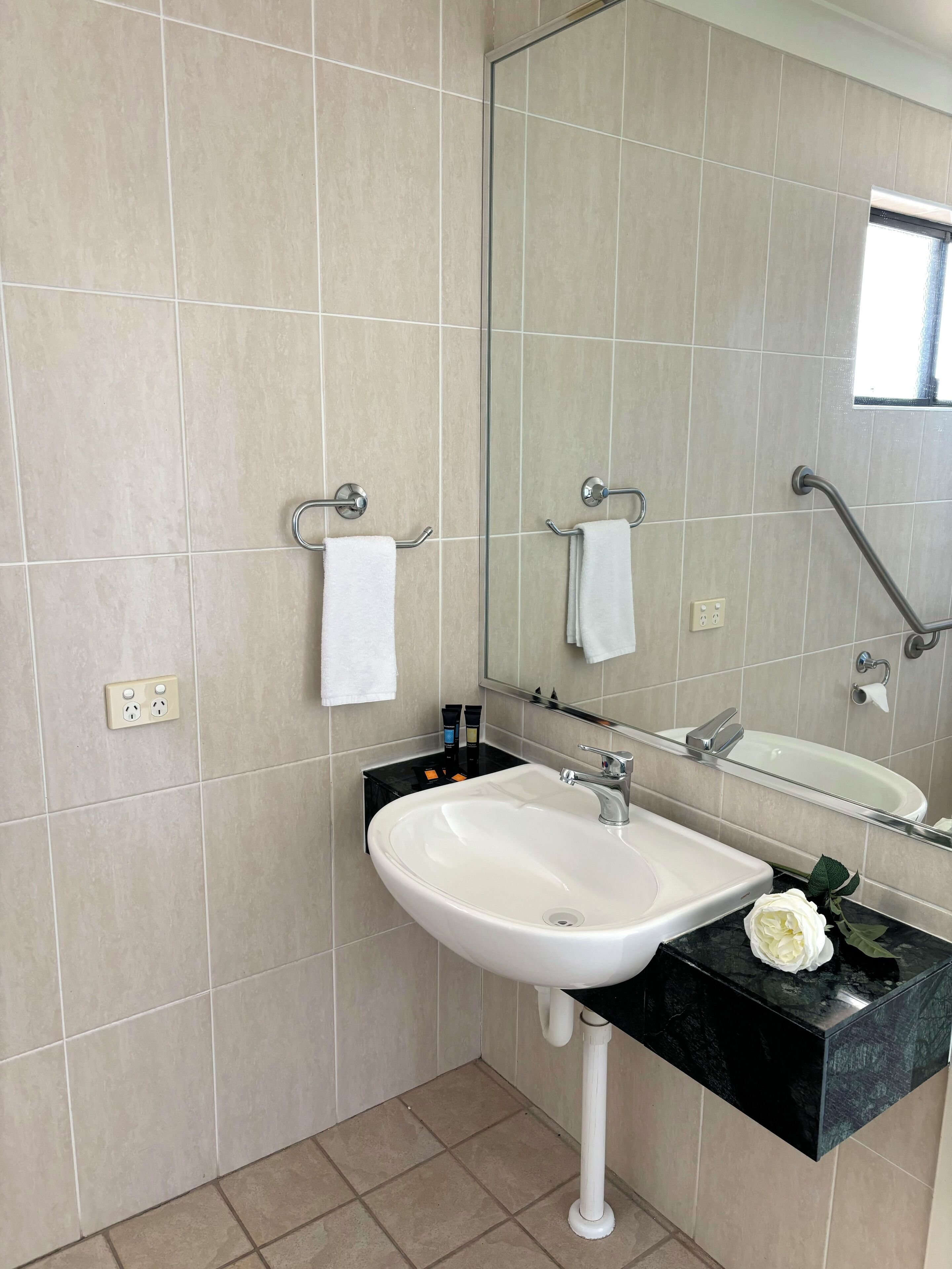 A bathroom with a white sink, black countertop, and a mirror above it. There are two towel racks, one with a white towel and another with a towel hanging on it.