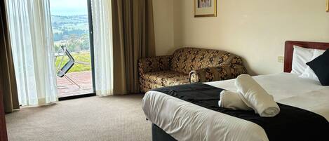 A hotel room with a large bed, a sofa, and a view through a sliding door.