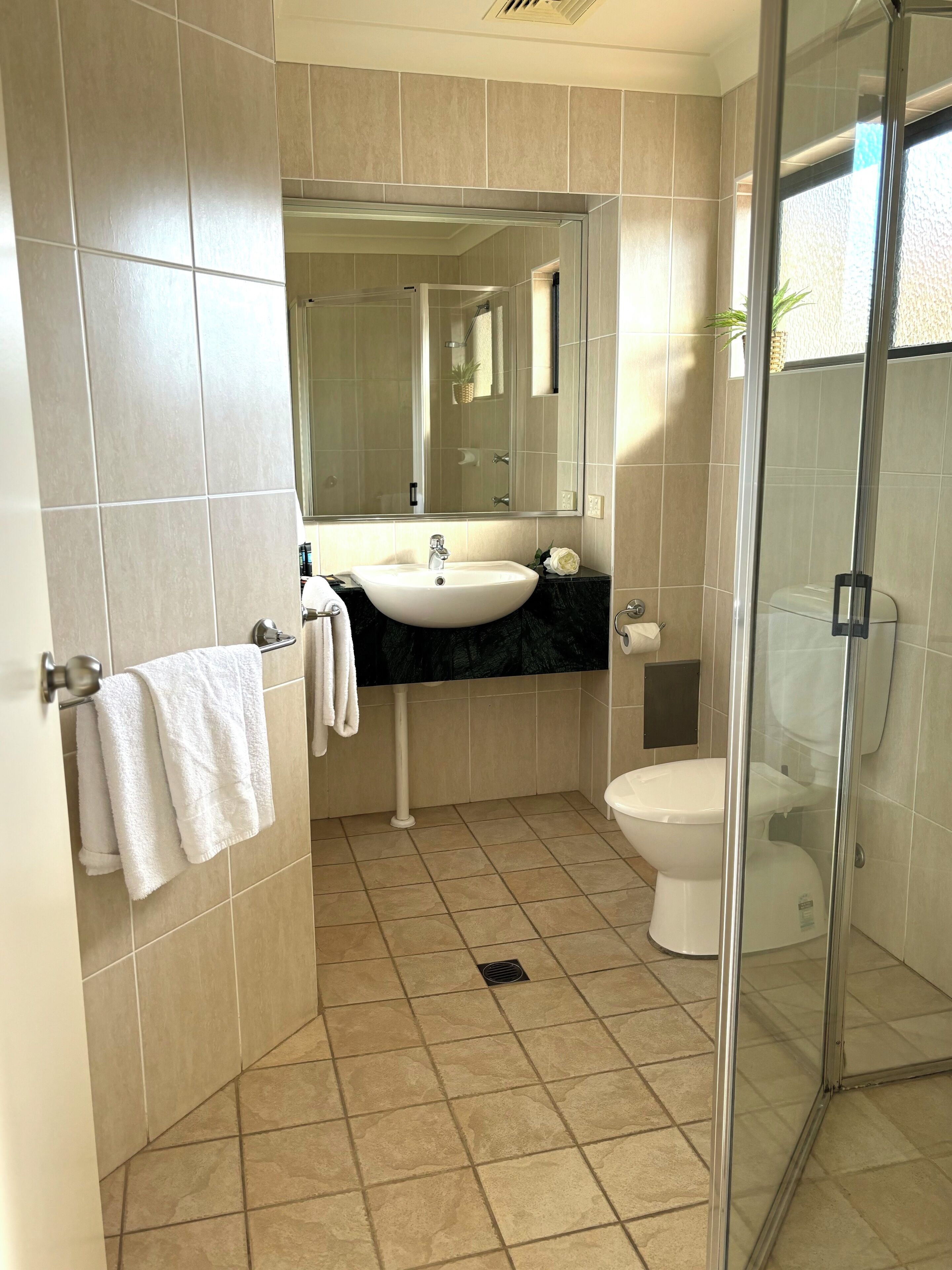A modern bathroom with a white sink, black countertop, and a glass shower enclosure.