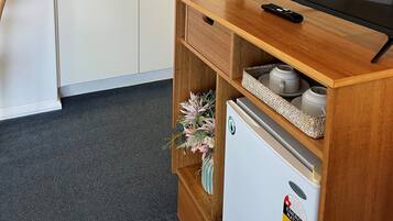 A compact kitchen with white cabinets, a microwave, a refrigerator, and a wooden TV stand with a remote.
