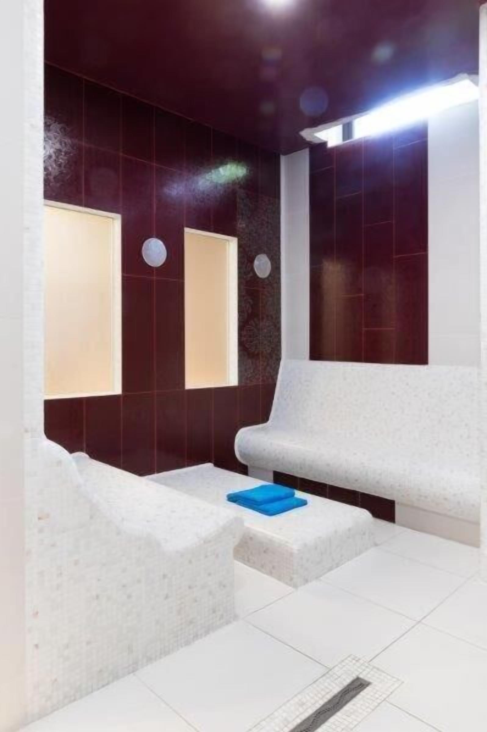 Een moderne badkamer met wandtegels in wit en donkerrood, een witte bank en een blauwe handdoek op een wit plateau.