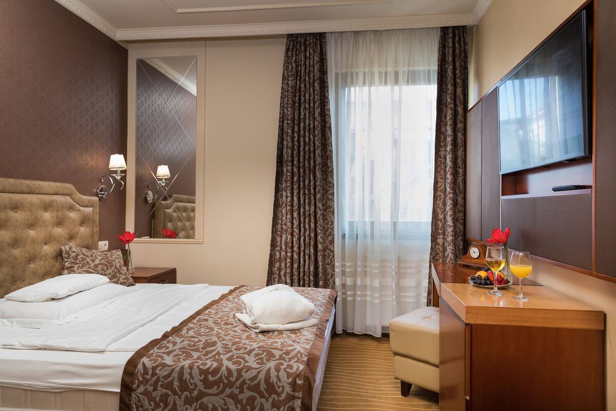 A hotel room with a large bed, a desk with a mirror, and a television.