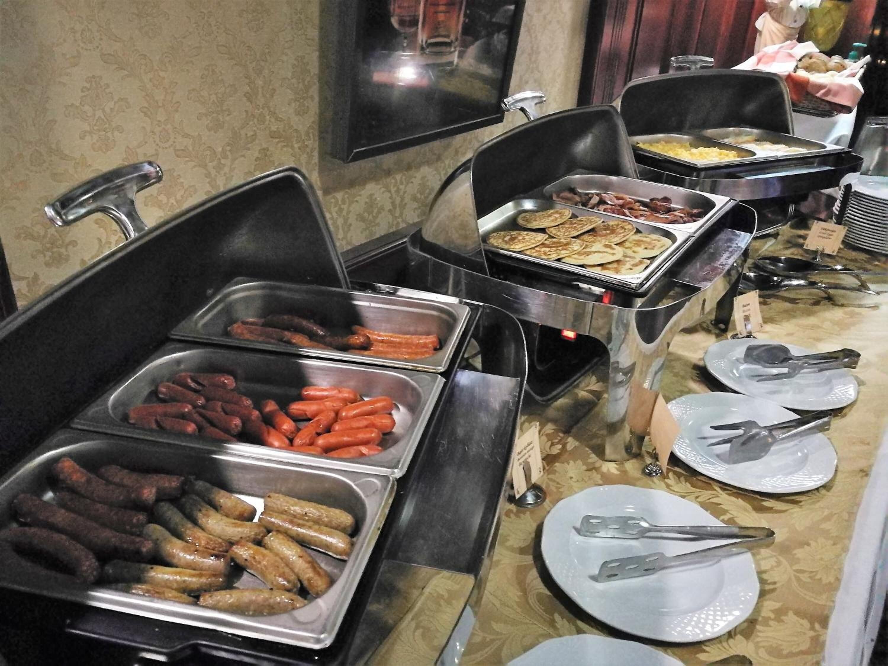 A buffet with various food options including sausages, hot dogs, and pancakes.