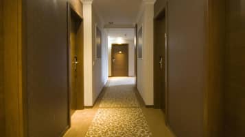 A hotel hallway with patterned carpet, wooden doors, and a light at the end.