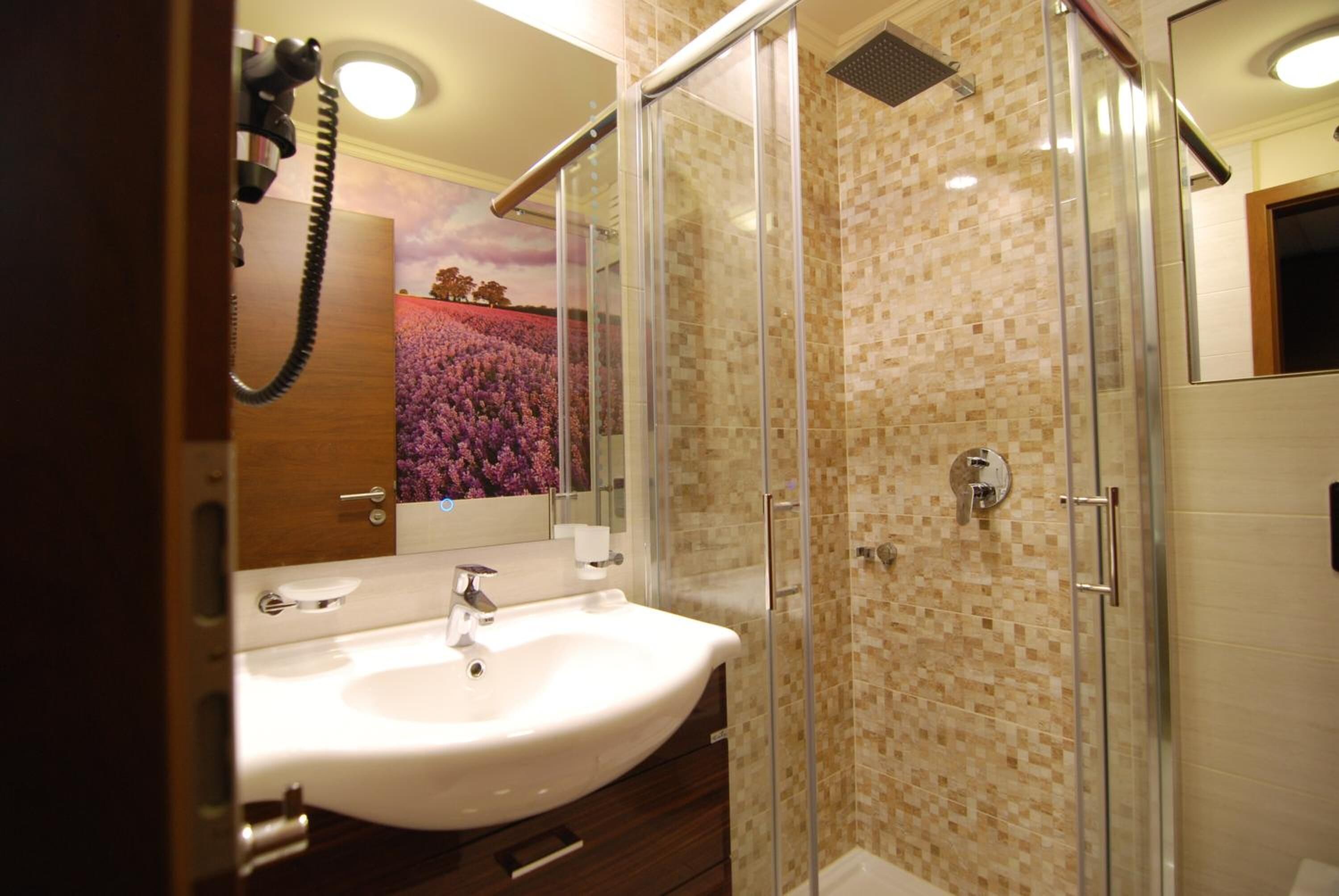 A bathroom with a glass shower enclosure, a white sink, and a mirror.