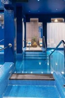 Una piscina interior con agua cristalina, escalones para entrar y una pequeña planta en los escalones.