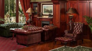 A traditional library with leather armchairs, a fireplace, and a large window overlooking a garden.