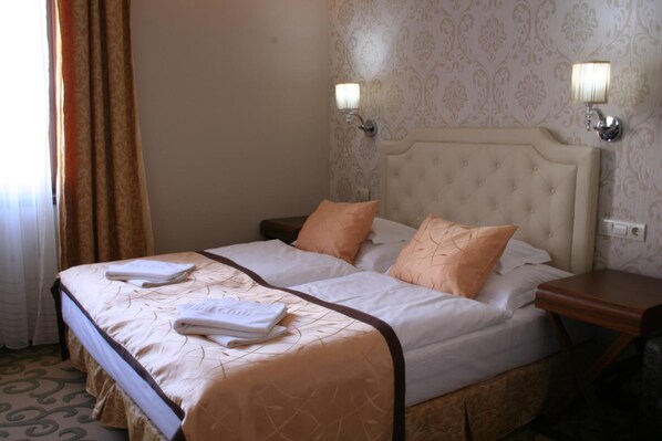 A double bed with a beige headboard and two pillows, a nightstand with a lamp, and a patterned carpet.