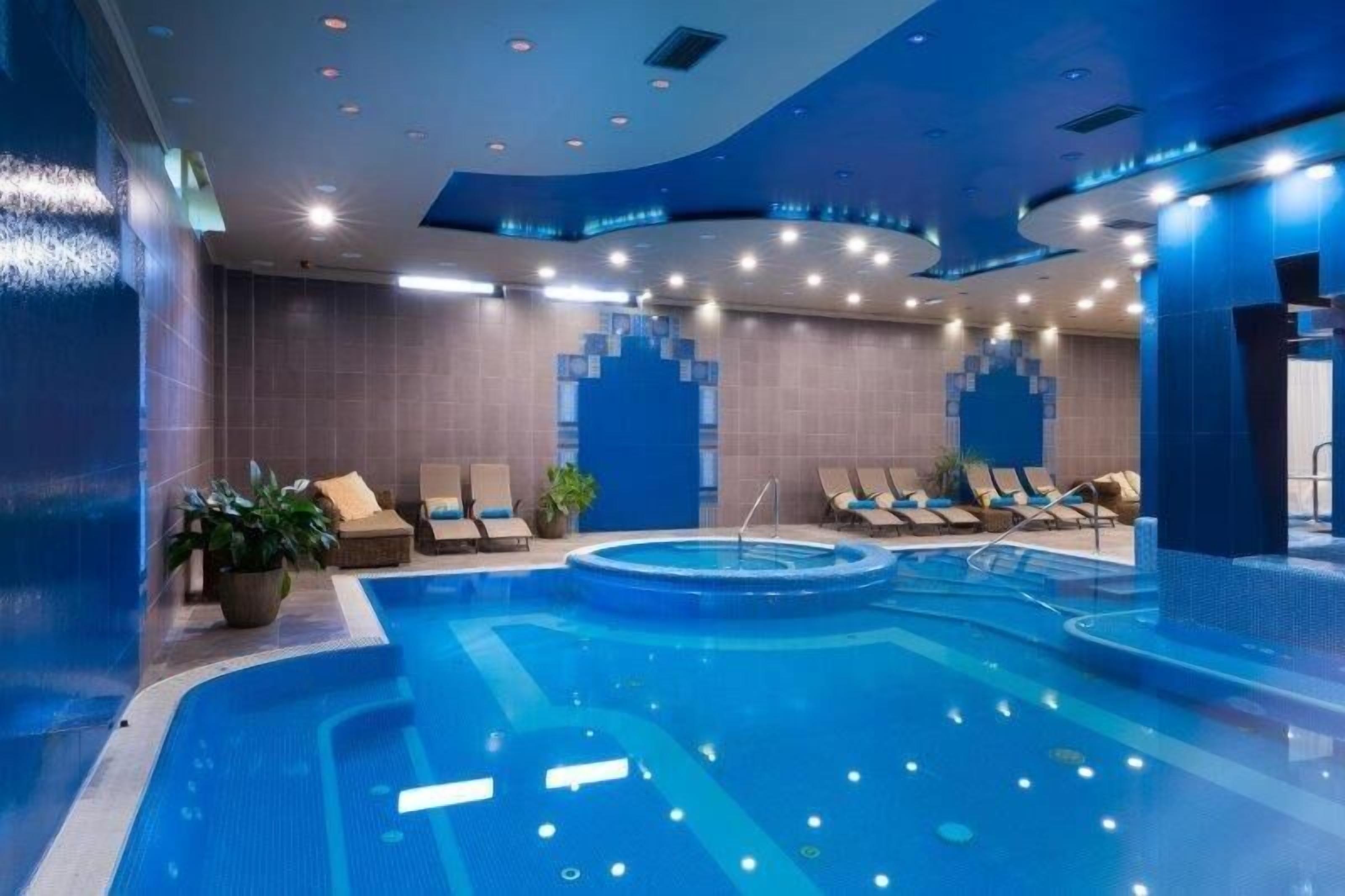 Piscina interna con sedie a sdraio e una piccola area con vasca idromassaggio.