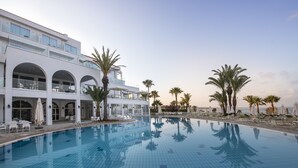 Een modern hotel met een groot zwembad, meerdere balkons en palmbomen.