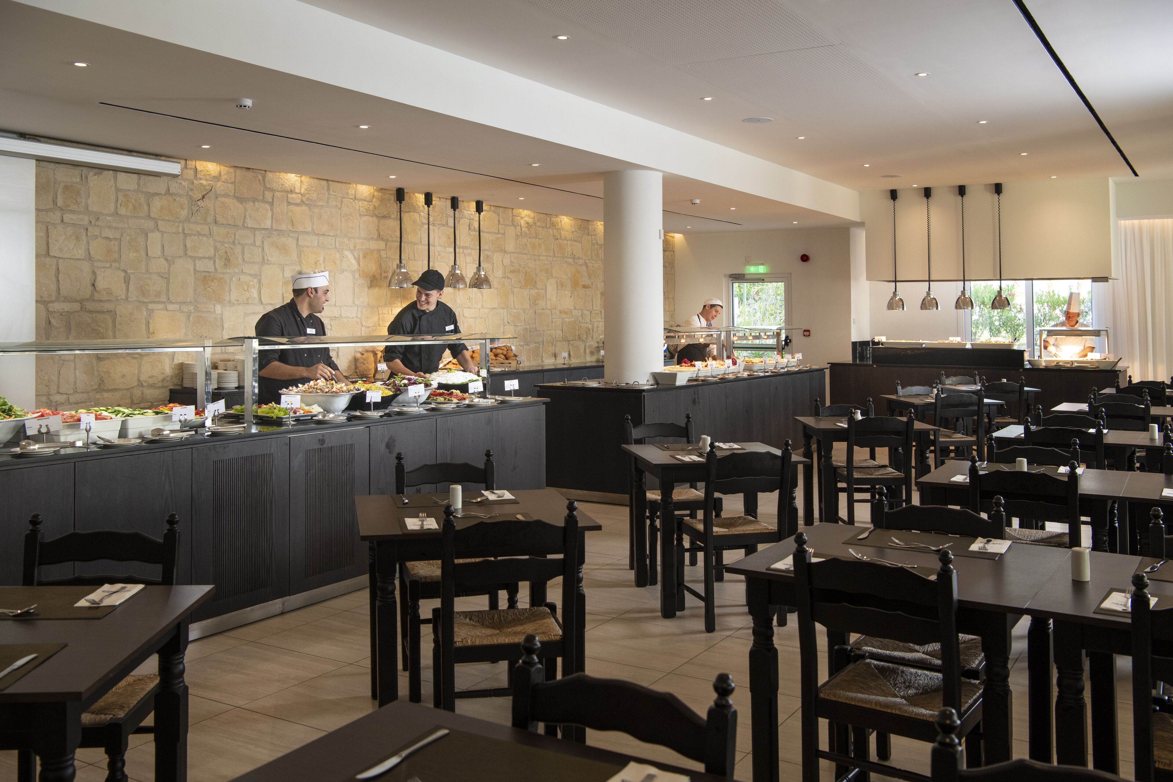 A buffet area with multiple food stations, a stone wall, and a seating area with tables and chairs.