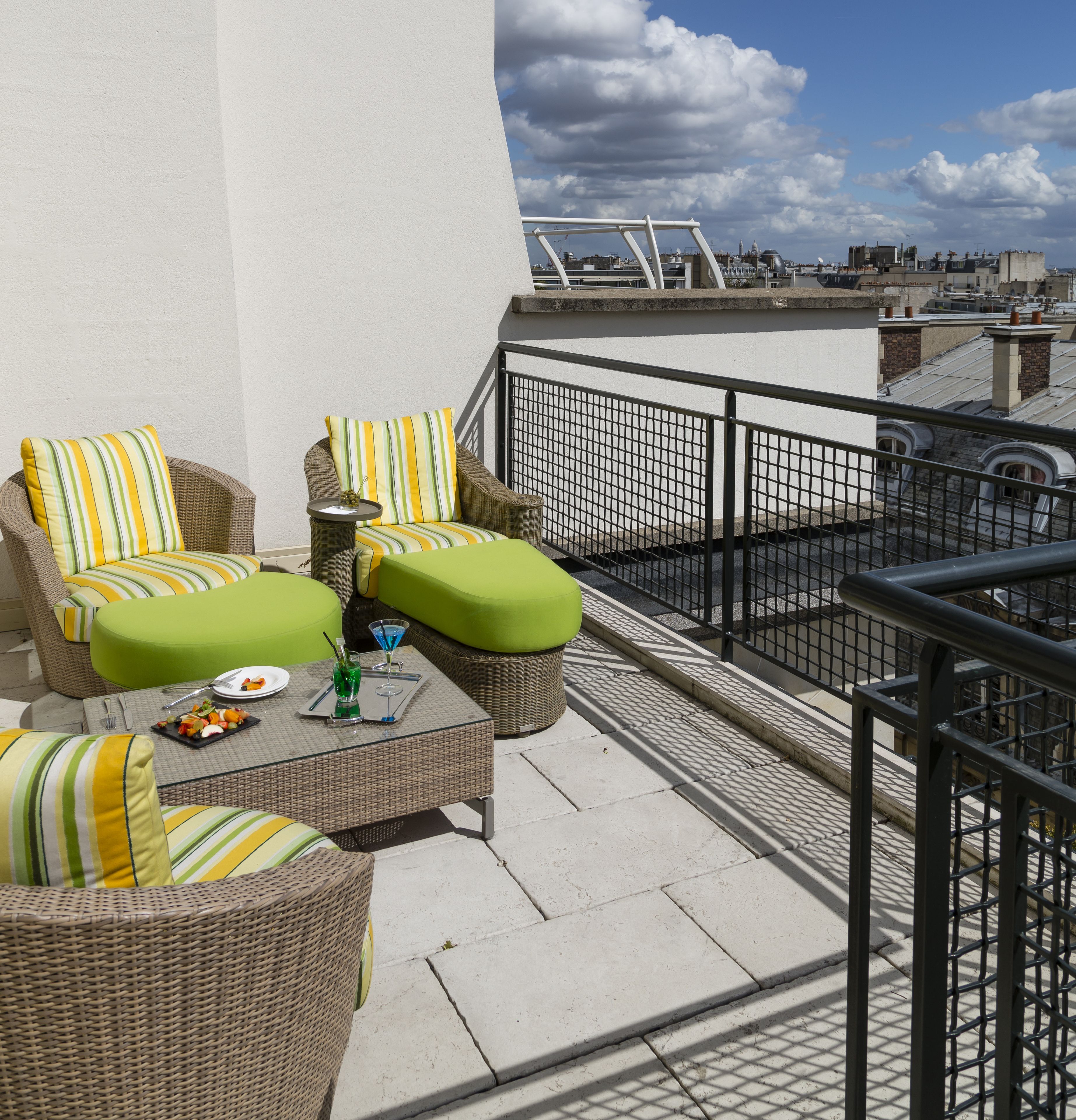 A rooftop terrace with wicker furniture, a dining table, and a view of the cityscape.