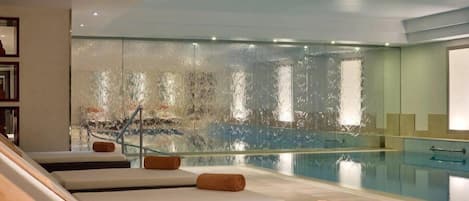 A spa area with a pool, lounge chairs, and a glass wall.