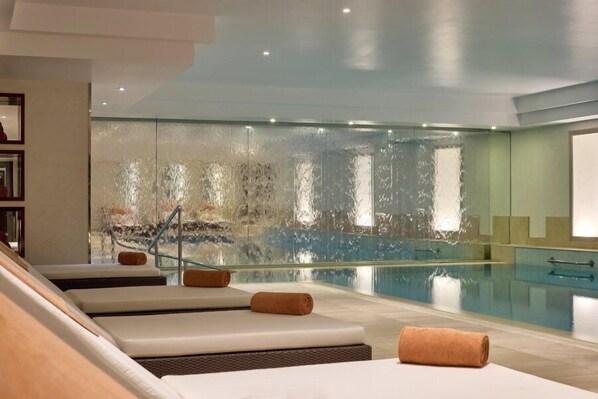 Ein Wellnessbereich mit Pool, Liegestühlen und einer Glaswand.