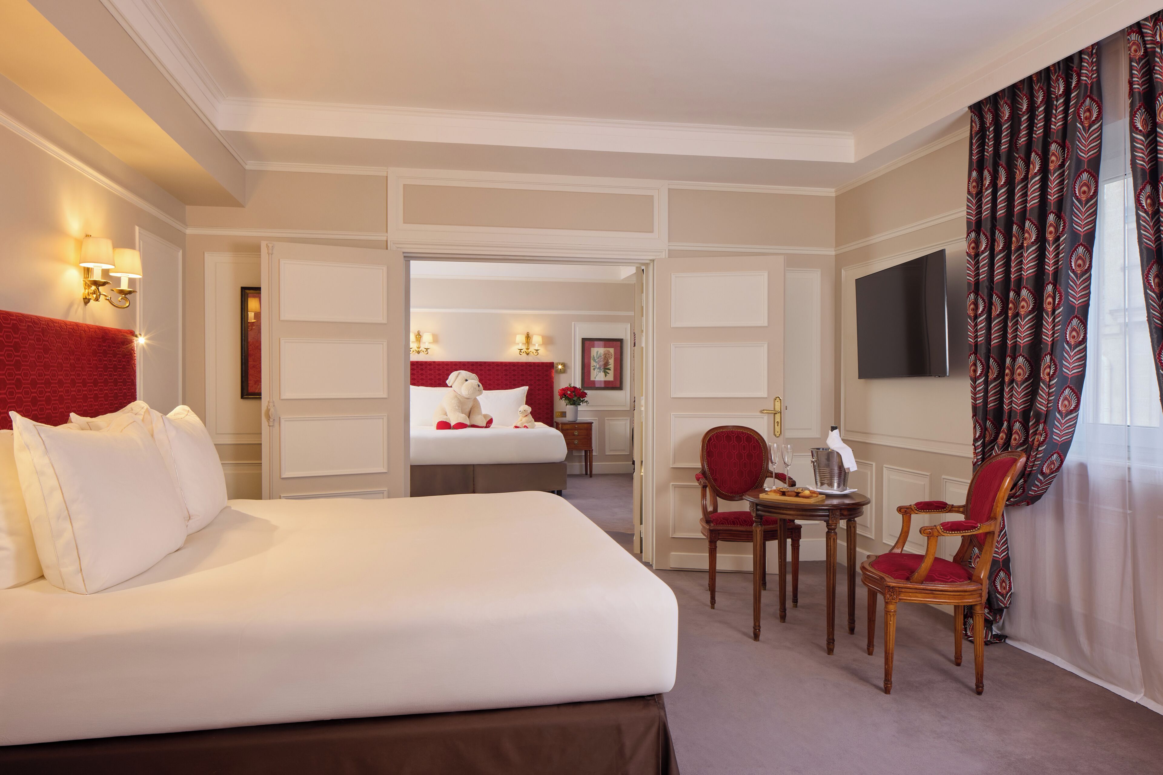 Habitación de hotel con una cama grande, una mesa de comedor con sillas, un televisor y una pared de acento roja.