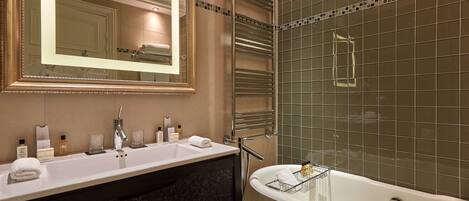 Une salle de bain moderne avec un grand miroir, un lavabo avec des articles de toilette et une baignoire sur pieds, accompagnée d’une serviette.