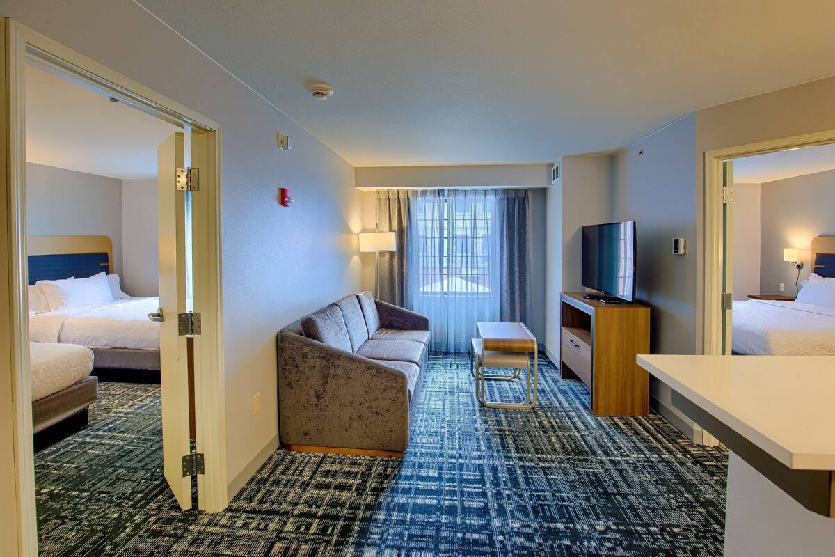A hotel room with a bed, sofa, TV, desk, and a patterned carpet.