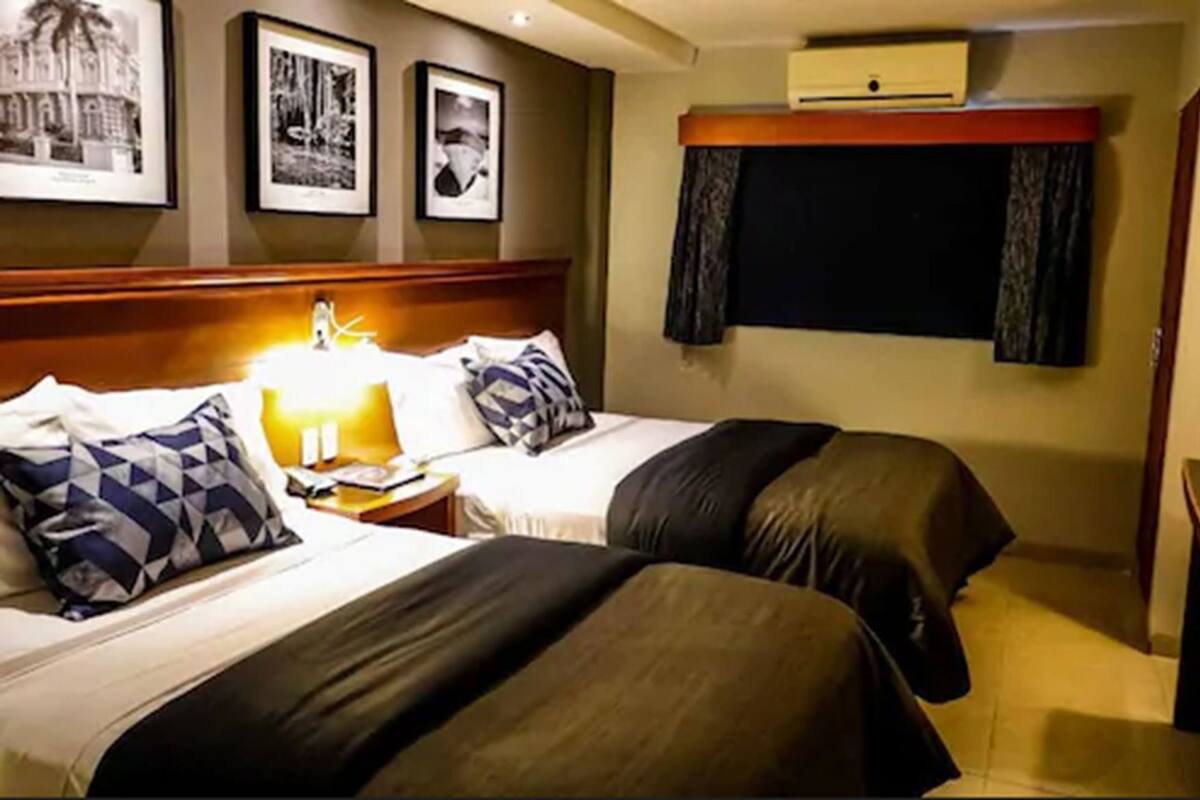 A hotel room with two beds, a nightstand with a lamp, and framed pictures on the wall.