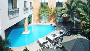 A swimming pool with lounge chairs and umbrellas, surrounded by buildings and greenery. - Hotel Nacional Merida (Mérida)