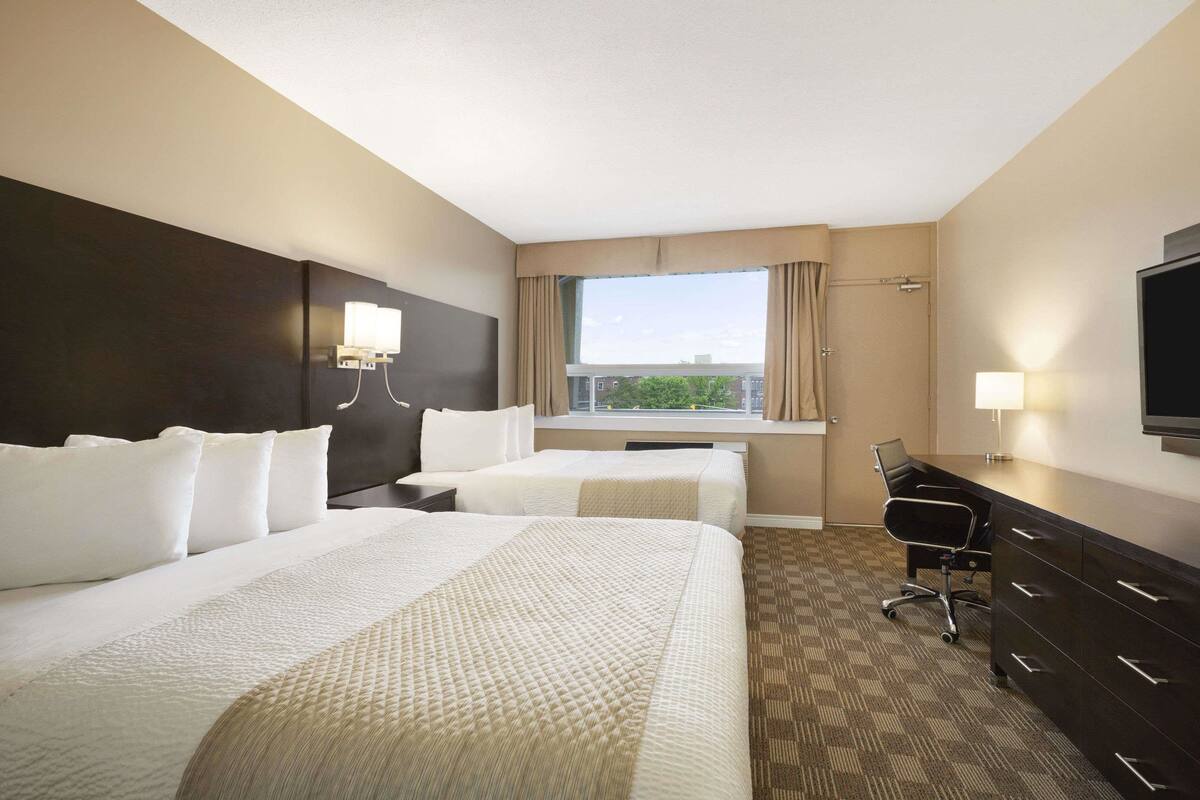 A hotel room with two beds, a desk, a chair, a TV, and a window with curtains.
