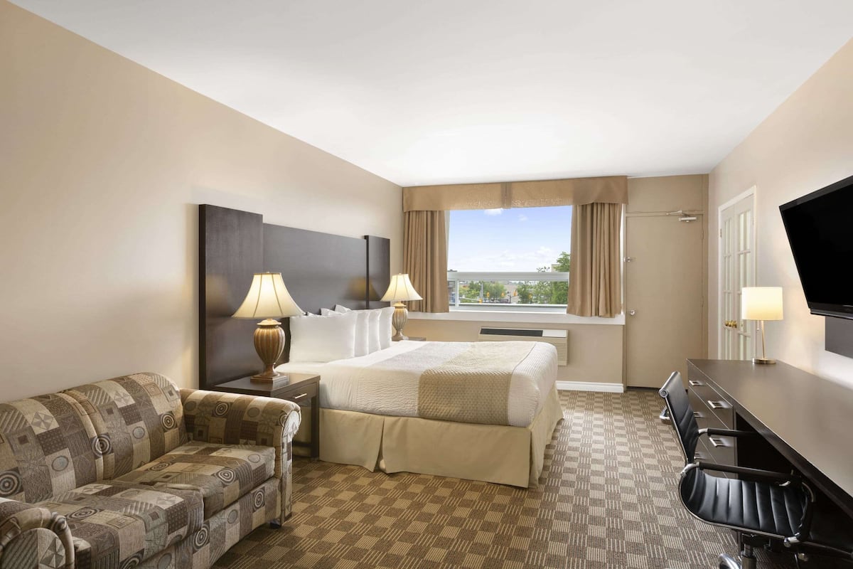A hotel room with a bed, a sofa, a desk, and a TV.