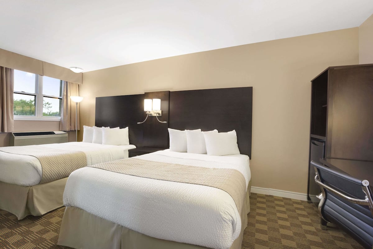 A hotel room with two beds, a large dark headboard, a flat-screen TV, and a window with curtains.