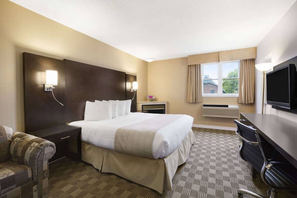 A hotel room with a large bed, a desk, a chair, a TV, and a window with curtains.