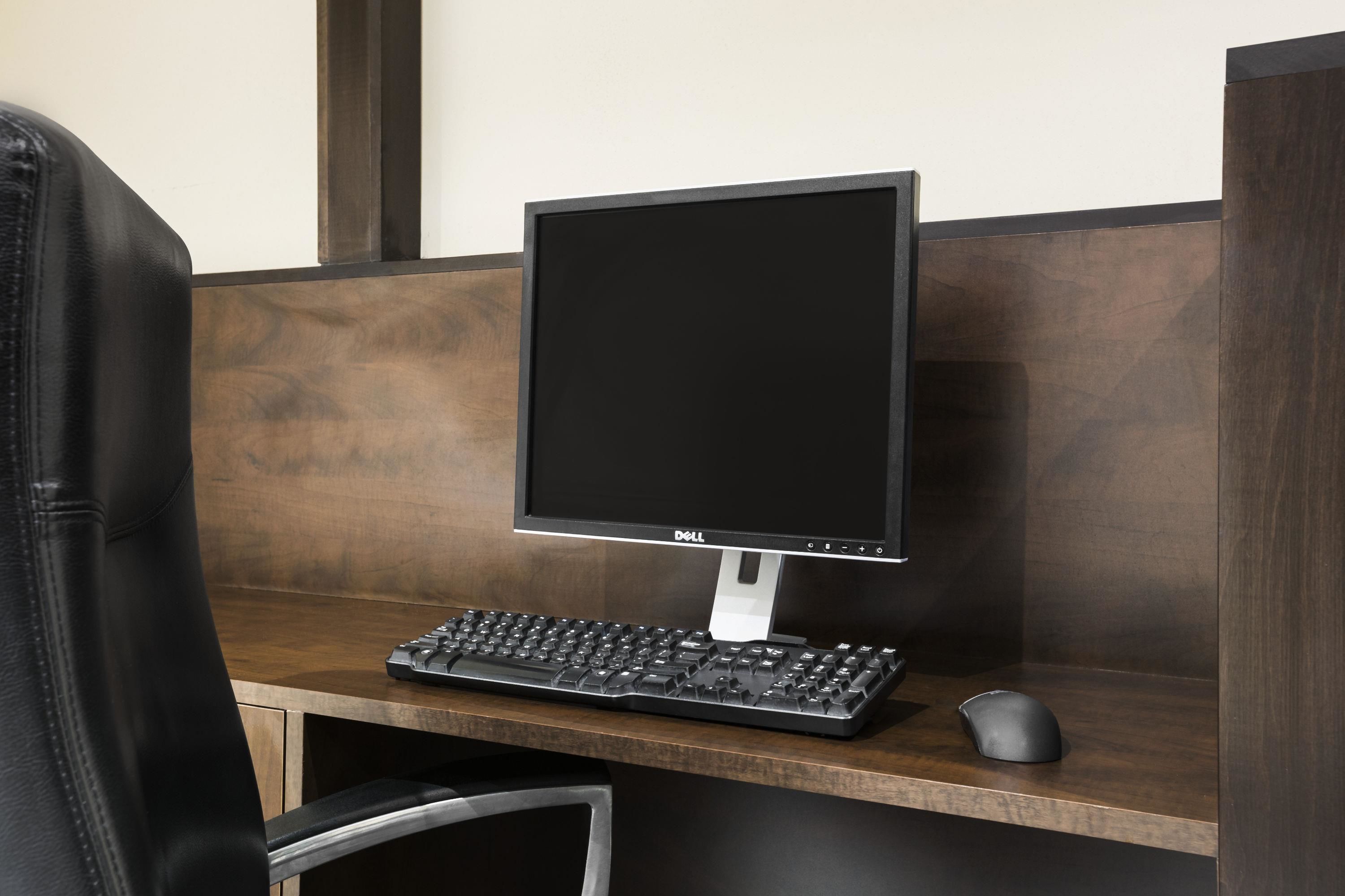 Un cubículo de oficina moderno con un monitor Dell, teclado y ratón sobre un escritorio de madera.